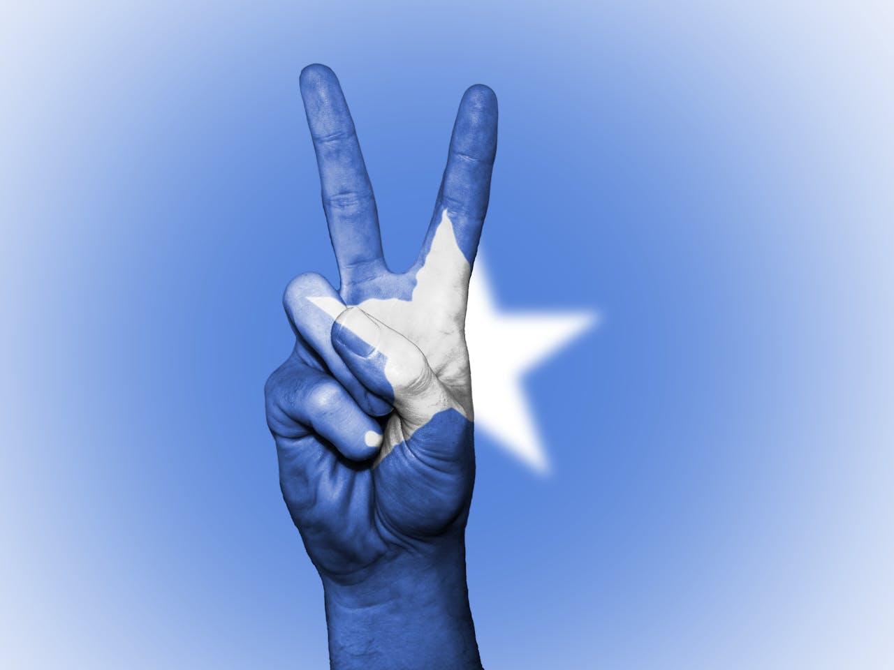 A hand making a peace gesture painted with the Somali flag colors, symbolizing national unity.